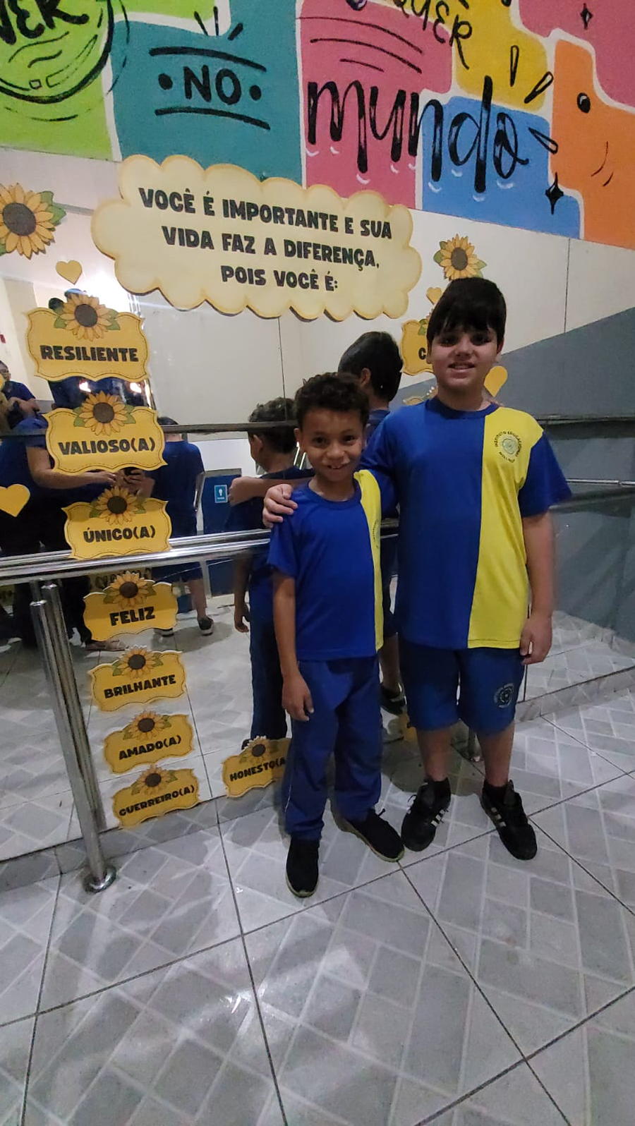 Dois alunos no corredor da escola, diante do mural de valores