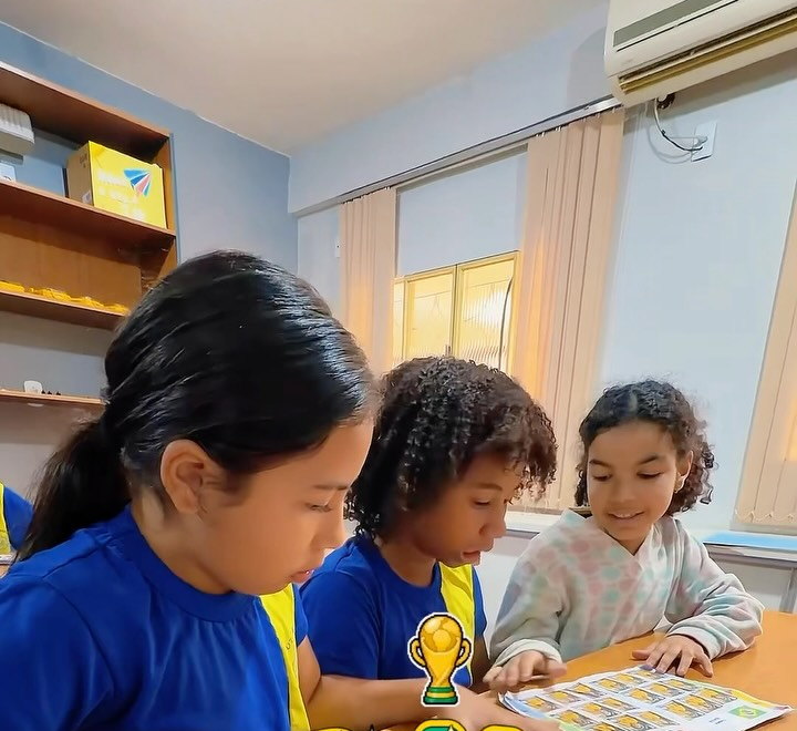 Três alunas do Fundamental I de uniforme trabalhando juntas em uma atividade sobre a carteira